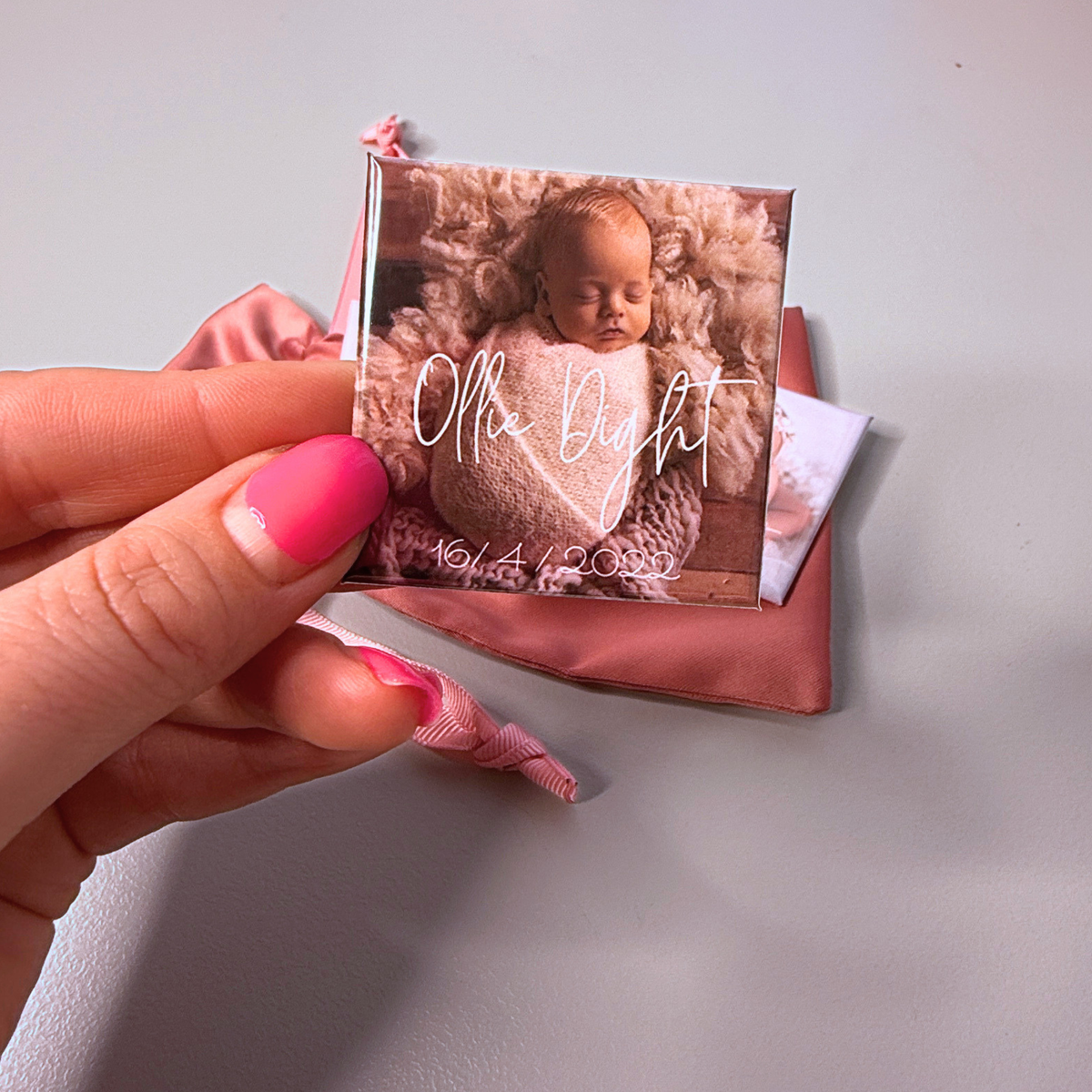 Hand holding personalised birth announcement photo magnet with sleeping newborn and pink satin pouch — custom baby keepsake magnet handmade in Melbourne Australia