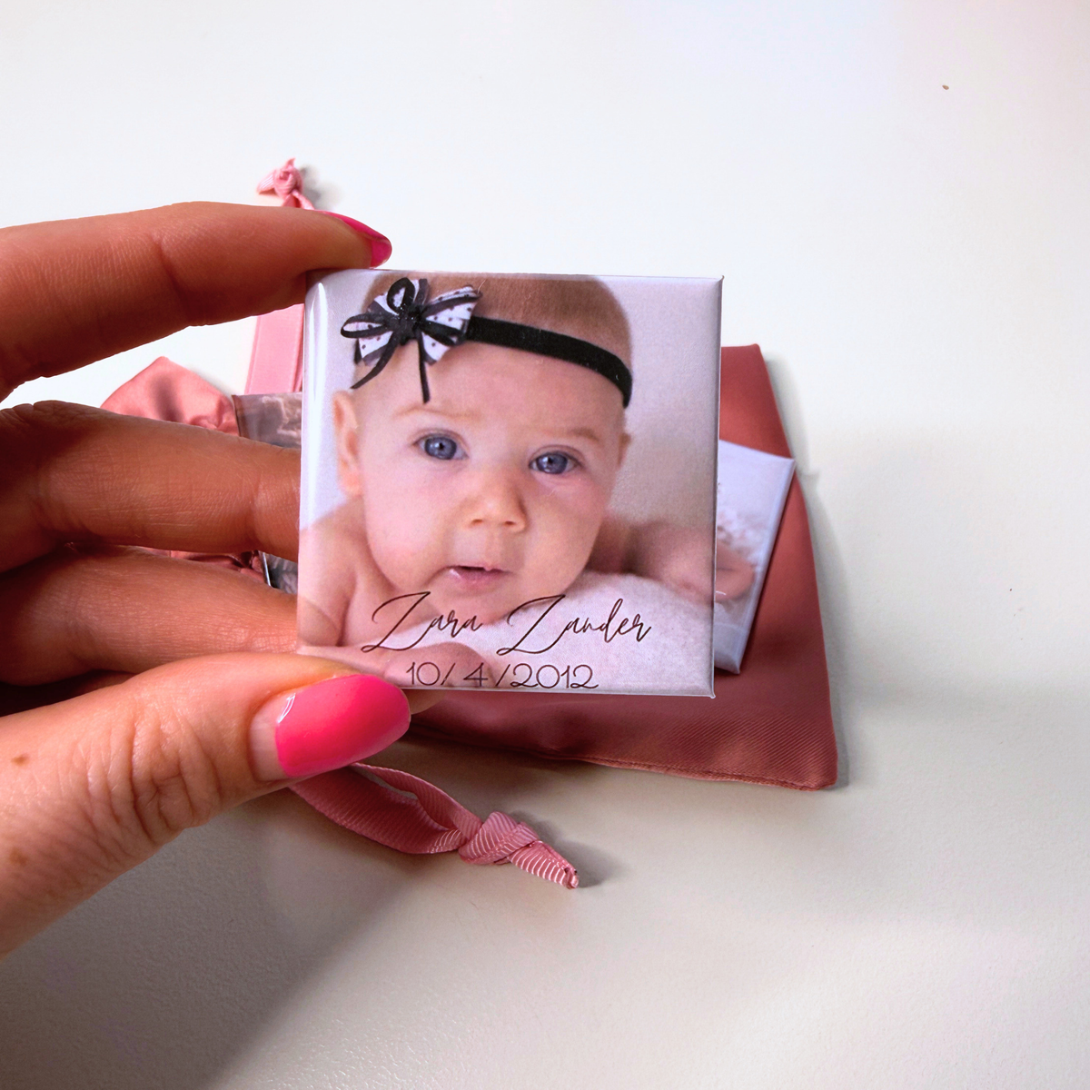 A hand holding a personalised birth announcement photo magnet featuring a baby’s portrait, name and birth date.