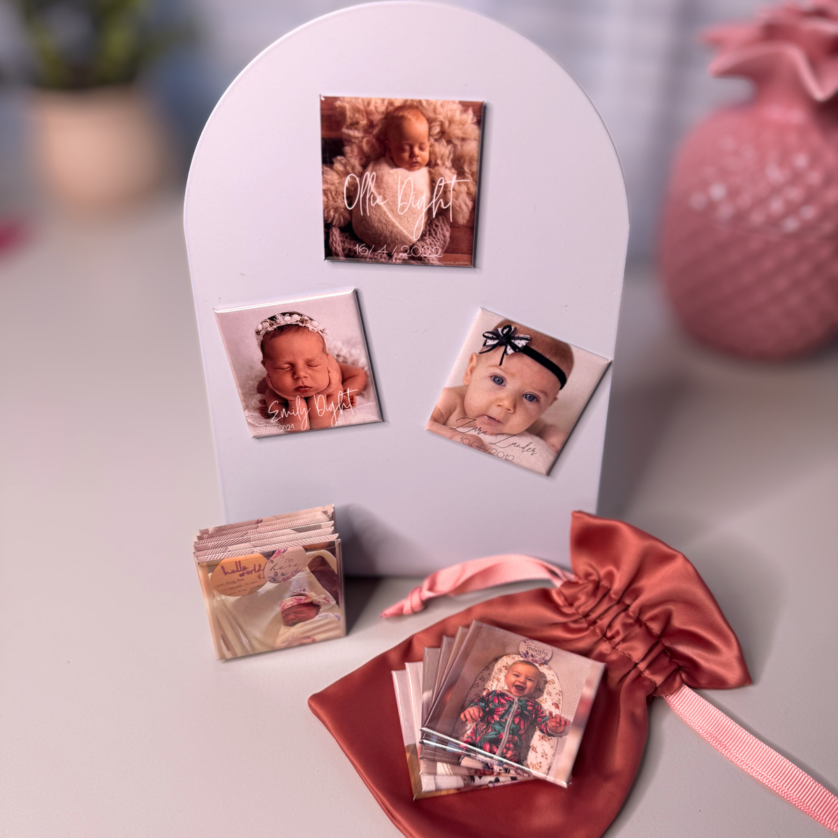 Birth announcement photo magnets displayed on white arch prop with satin pouch and milestone magnet stacks — personalised newborn keepsake magnets handmade in Melbourne Australia