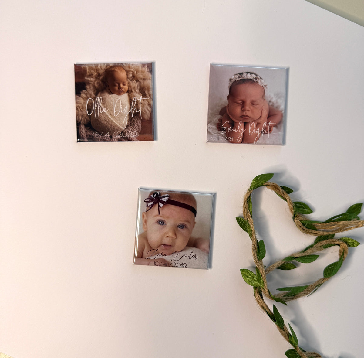 Three personalised birth announcement photo magnets on white wall with green vine heart — custom newborn keepsake magnets handmade in Melbourne Australia