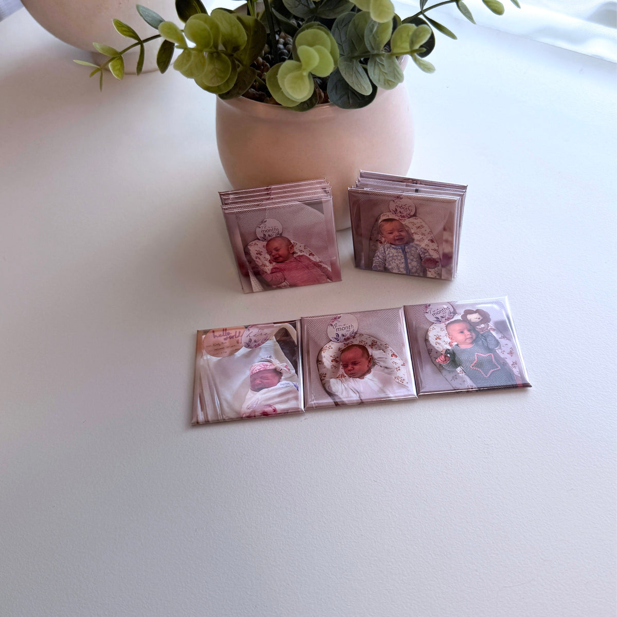 Stacked sets of custom baby milestone magnets on white table with plant — personalised newborn to baby magnets handmade in Melbourne Australia