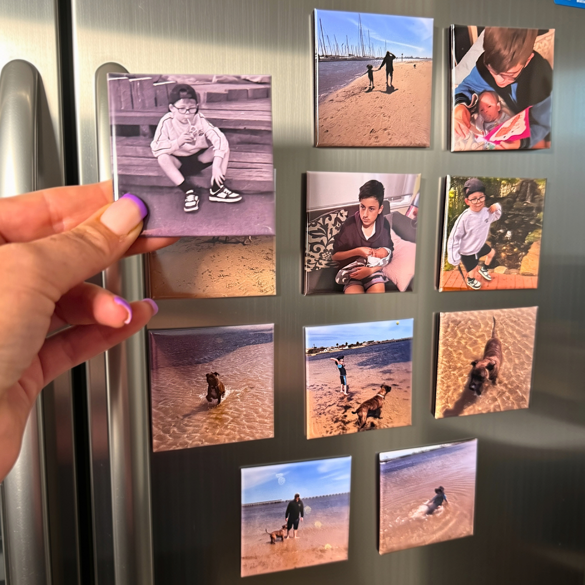 Hand holding a custom square photo magnet in front of a fridge covered with personalised photo magnets — handmade in Melbourne
