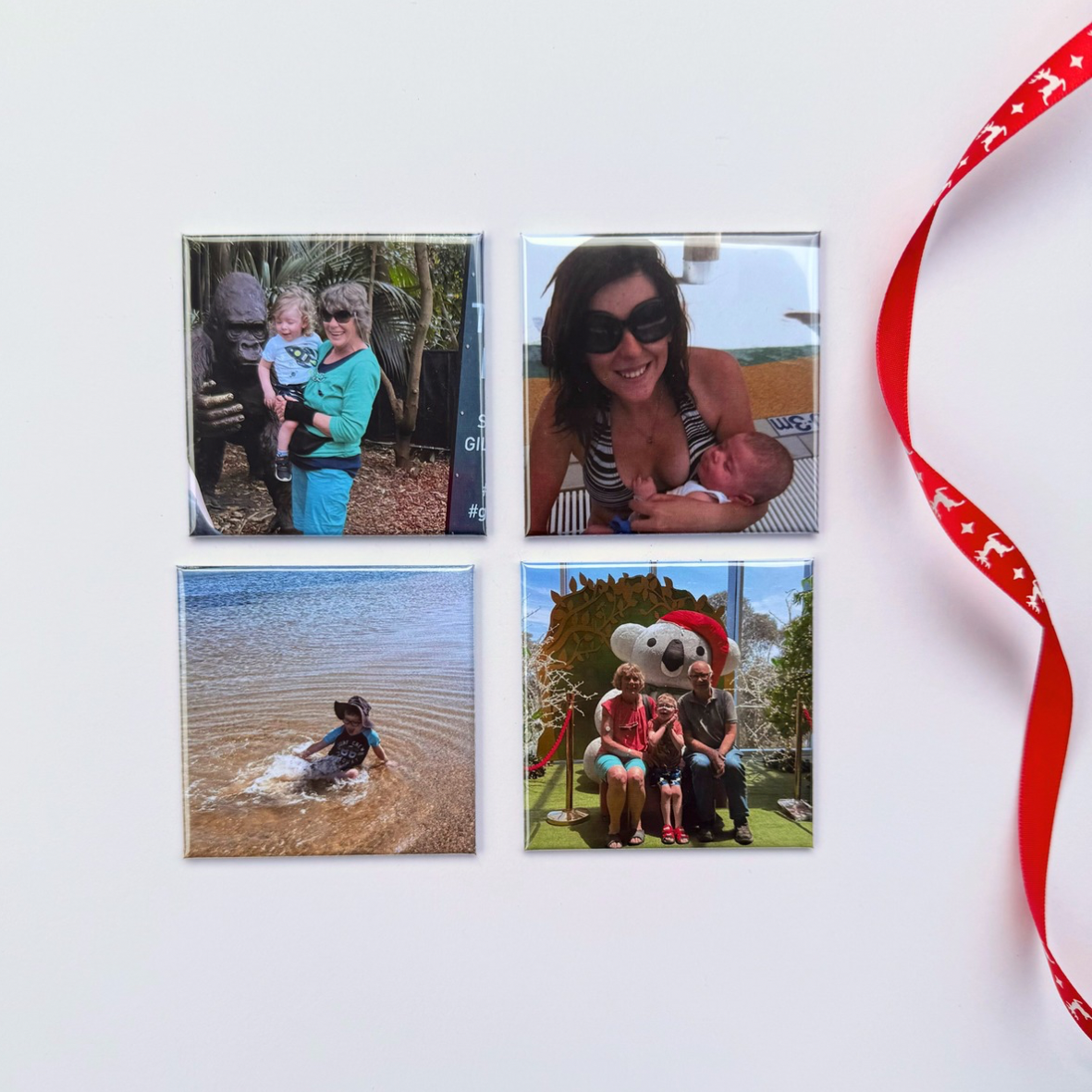  Four square photo magnets displaying family memories on a cream background beside a red Christmas ribbon.