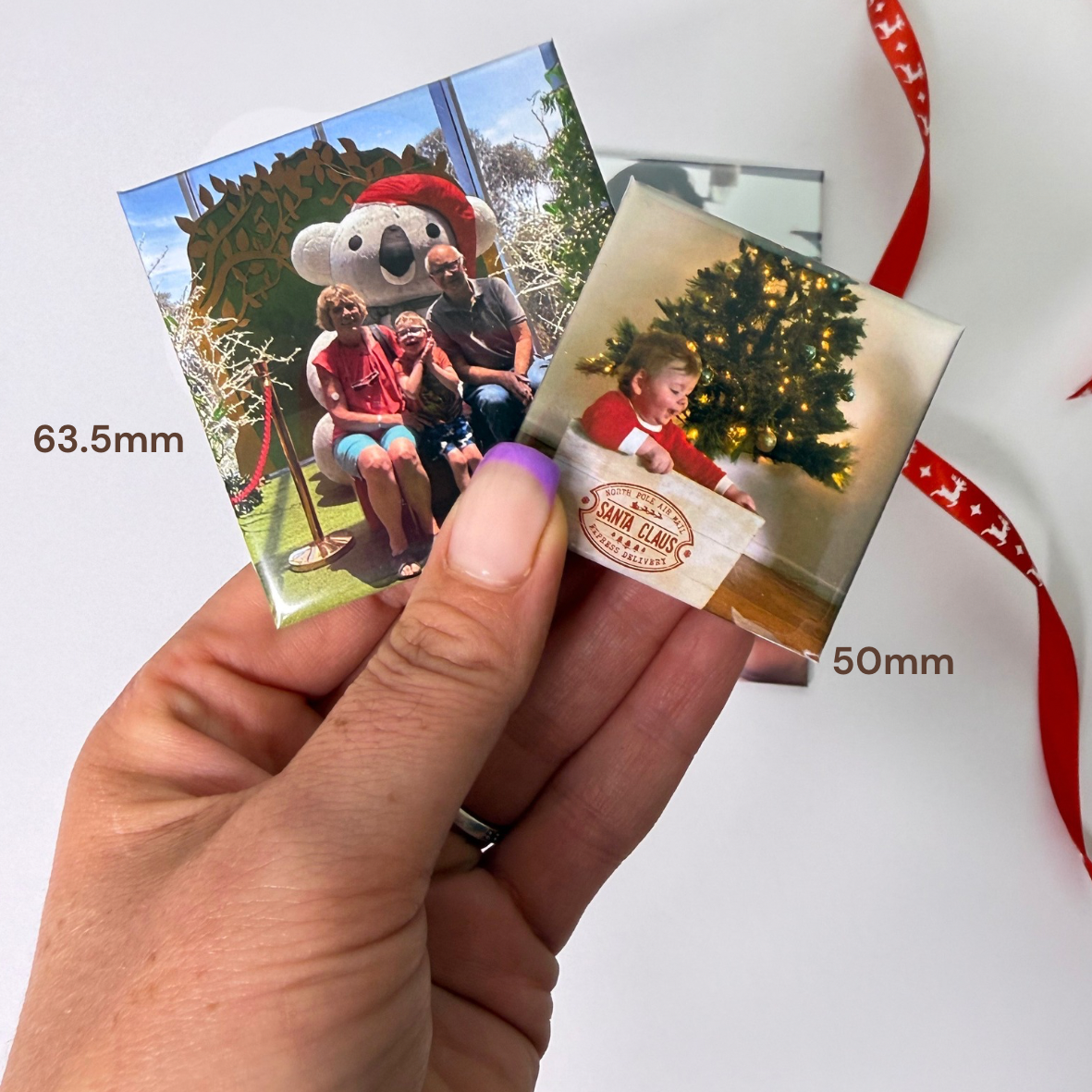 Hand holding 50 mm and 63.5 mm square photo magnets side by side to compare their sizes