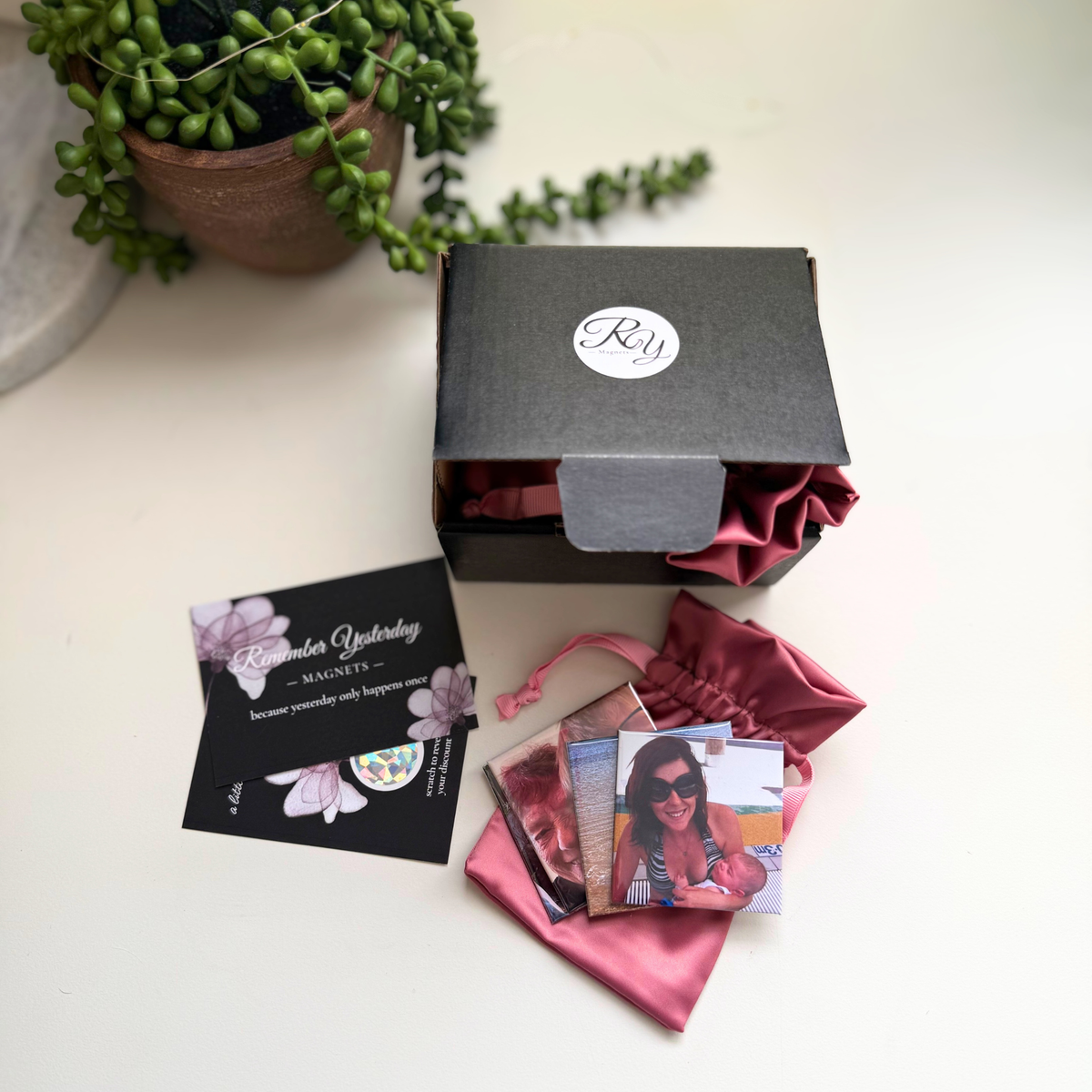 Photo magnets on a pink satin pouch beside a black gift box and Remember Yesterday Magnets branded cards.