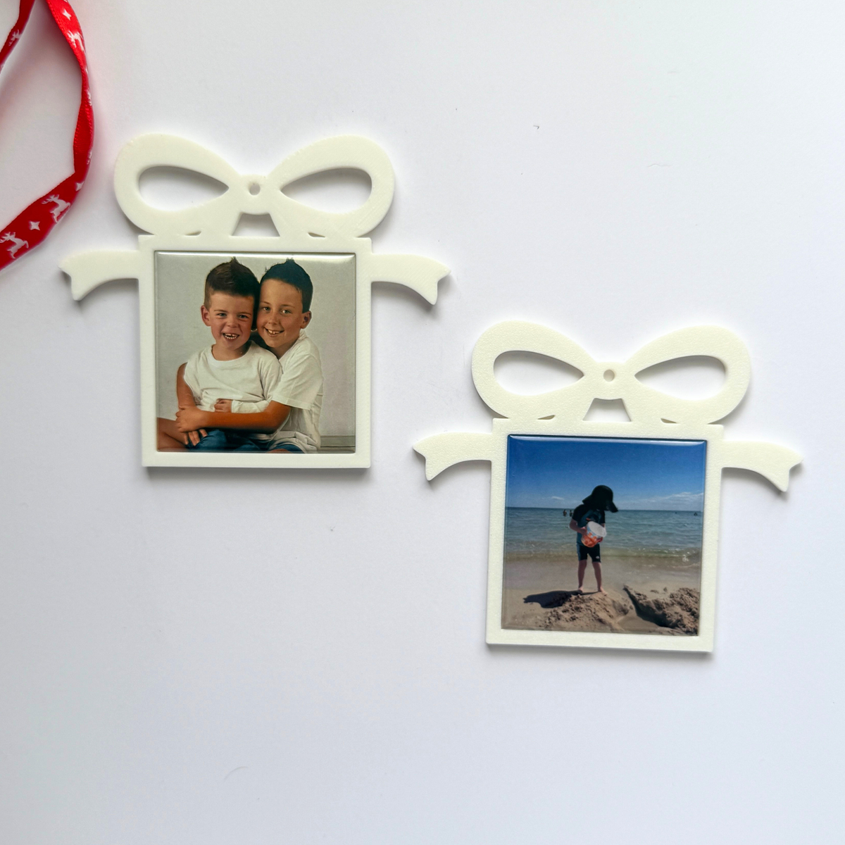 Two white present-shaped photo magnet ornaments on a light background, one with two smiling boys and one with a beach photo.